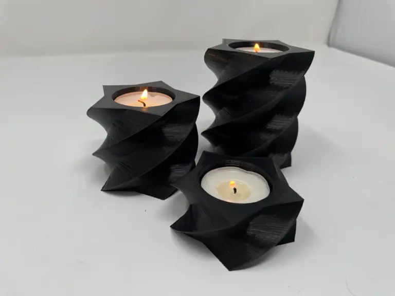 Drei schwarze 3D-gedruckte Teelichthalter mit gedrehter Form und brennenden Teelichtern