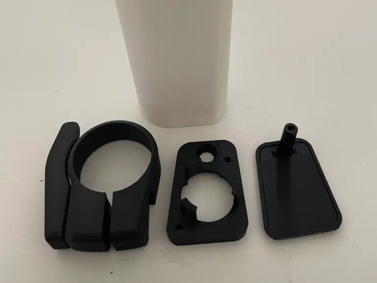 Schwarze 3D-gedruckte Schelle und Halteplatten vor einem weißen Rohr