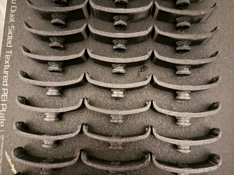 Schwarze 3D-gedruckte Bauteile in Reihen auf einer Druckplatte