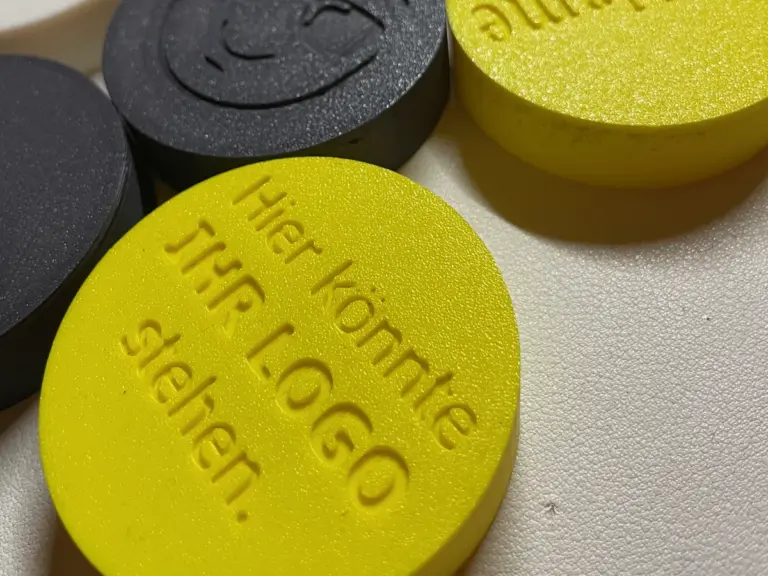 Runde 3D-gedruckte Dosendeckel in Gelb und Grau mit der Prägung „Hier könnte Ihr Logo stehen“