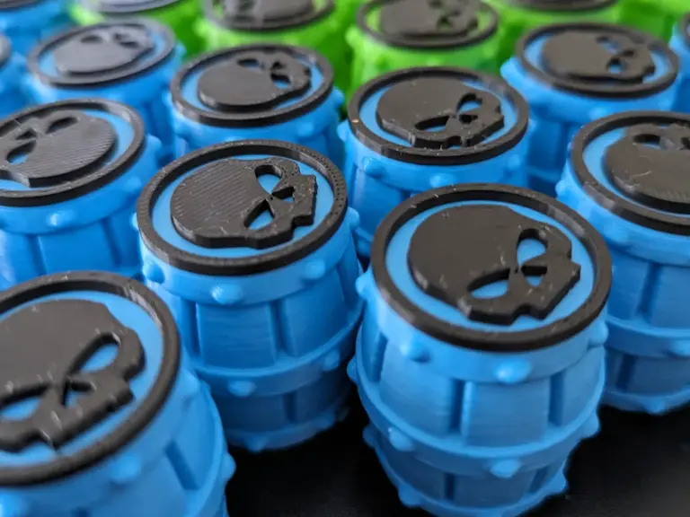 Blaue und grüne 3D-gedruckte Spielsteine in Fassform mit schwarzem Totenkopf-Emblem