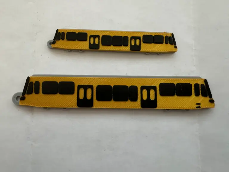 Zwei gelb-schwarze 3D-gedruckte Anhänger in Form einer Stadtbahn